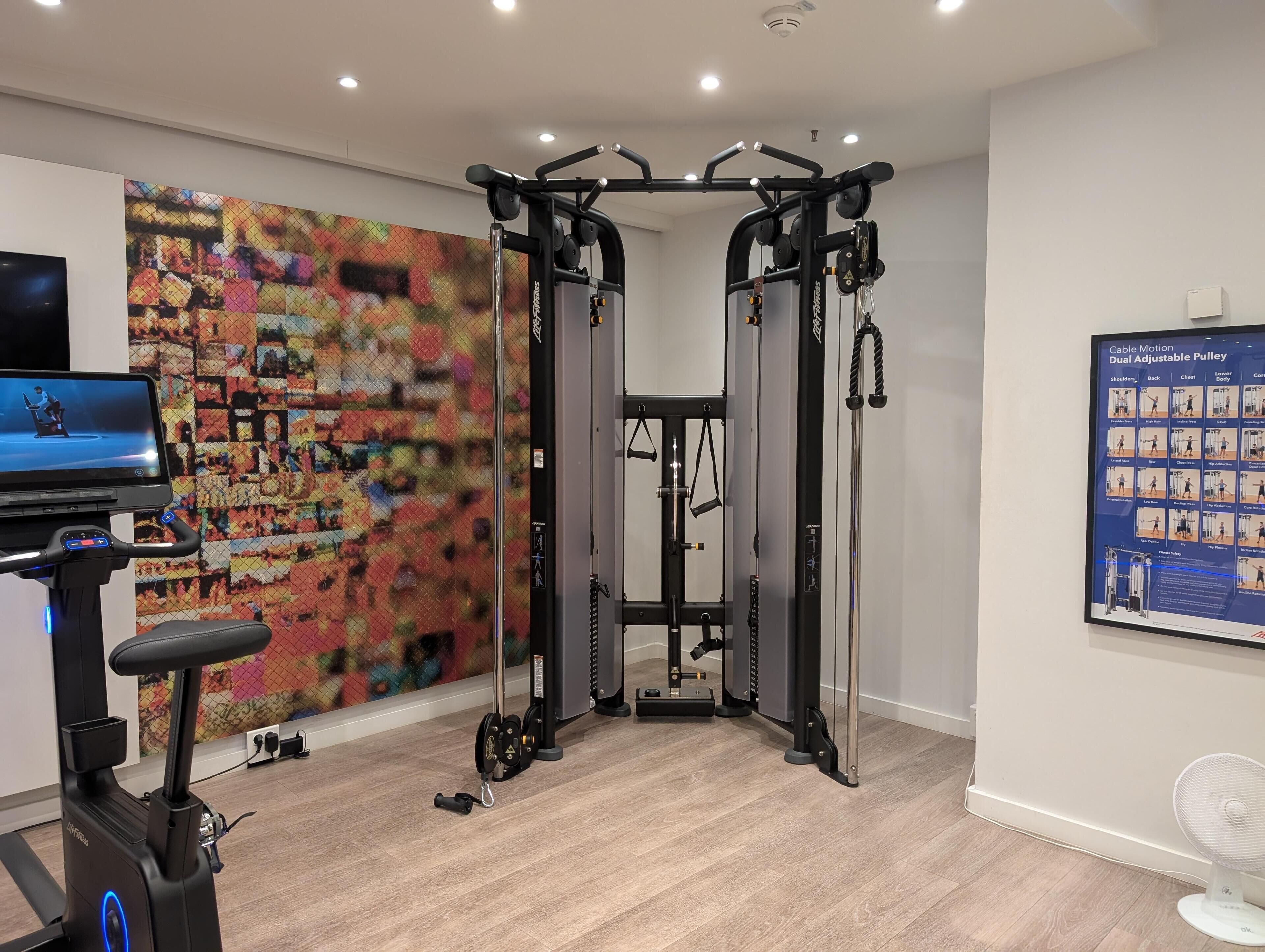 A home gym with a cable machine, a stationary bike, and a TV screen.