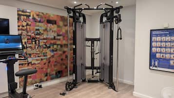 A home gym with a cable machine, a stationary bike, and a TV screen.