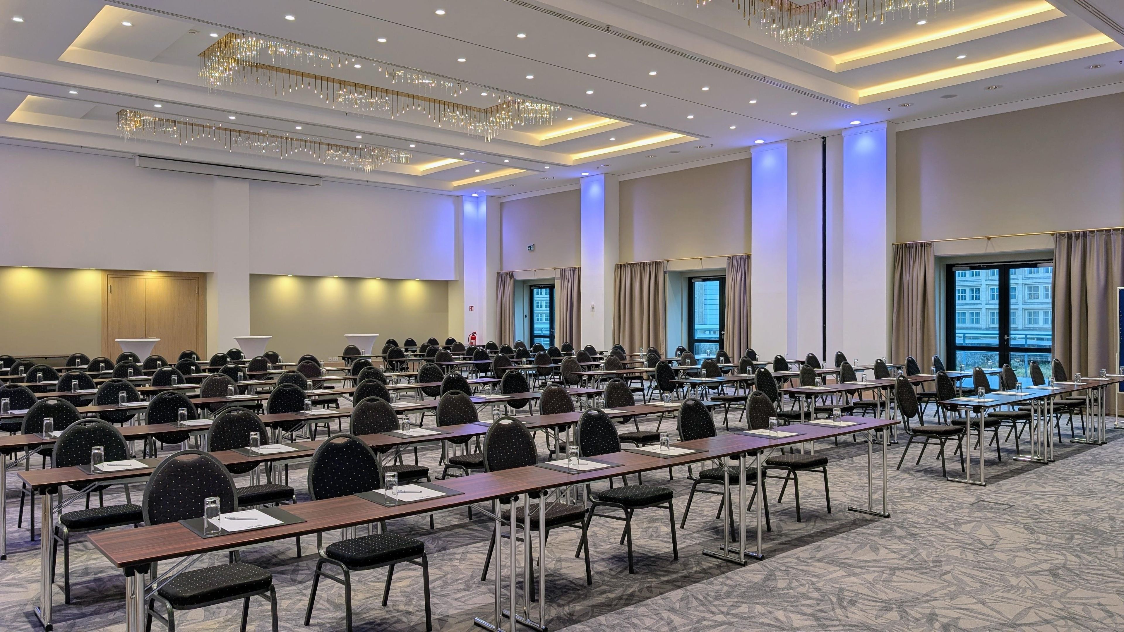 A conference room with rows of tables and chairs, a chandelier, and large windows.