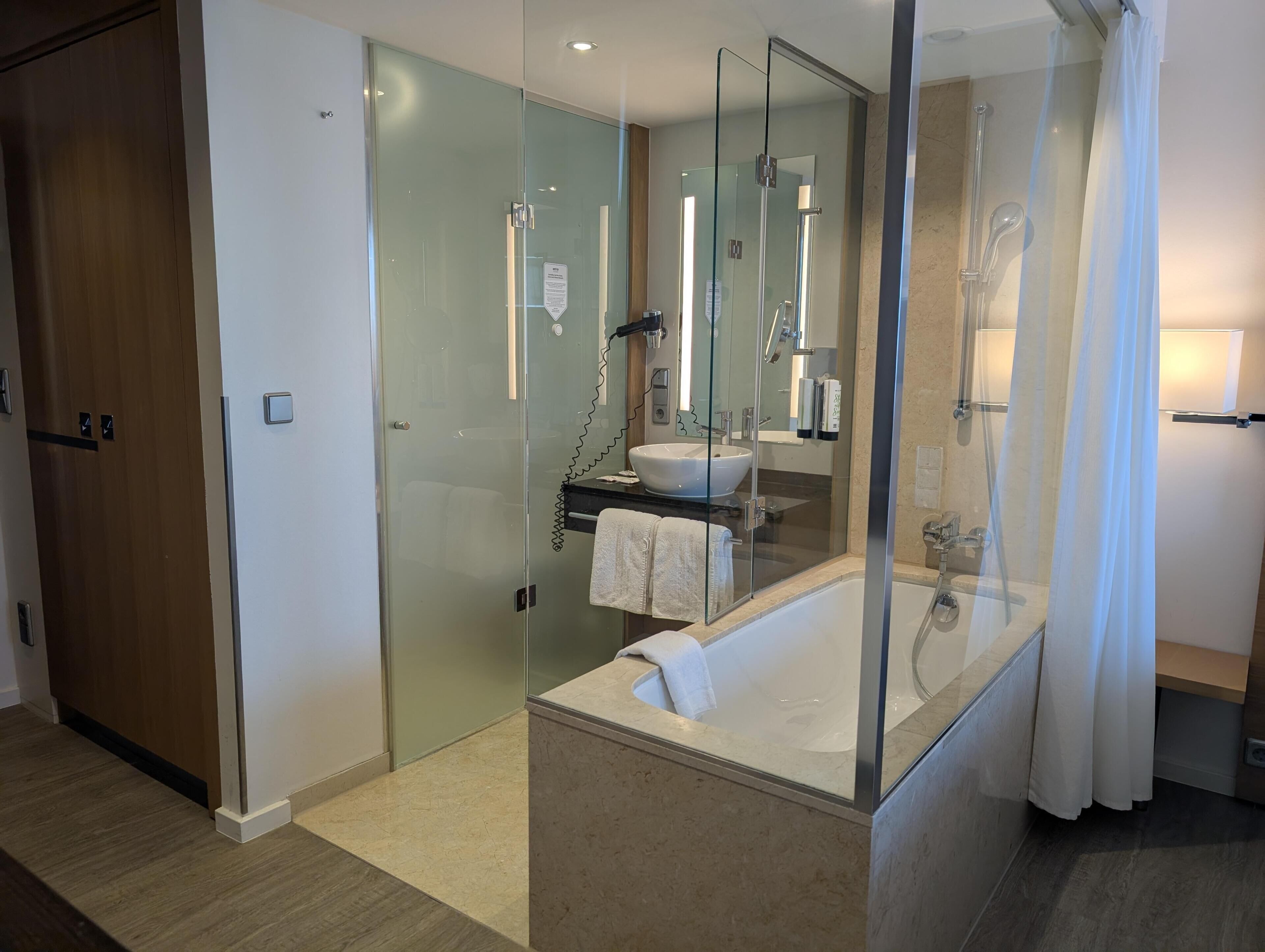 Un baño moderno con ducha envuelta en cristal, un espejo grande y una bañera blanca.
