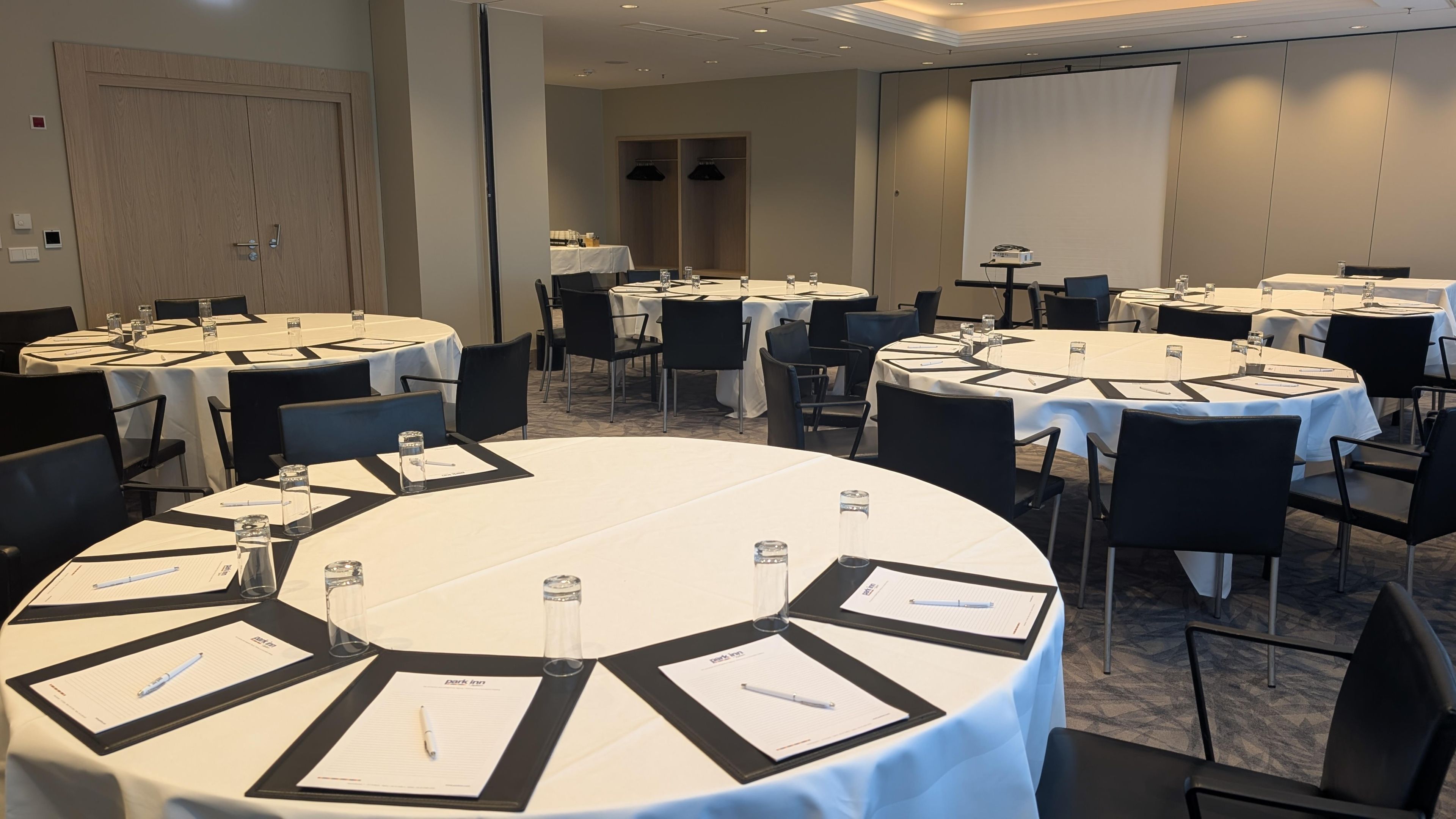 A conference room with multiple round tables, each with name cards, pens, and water glasses.