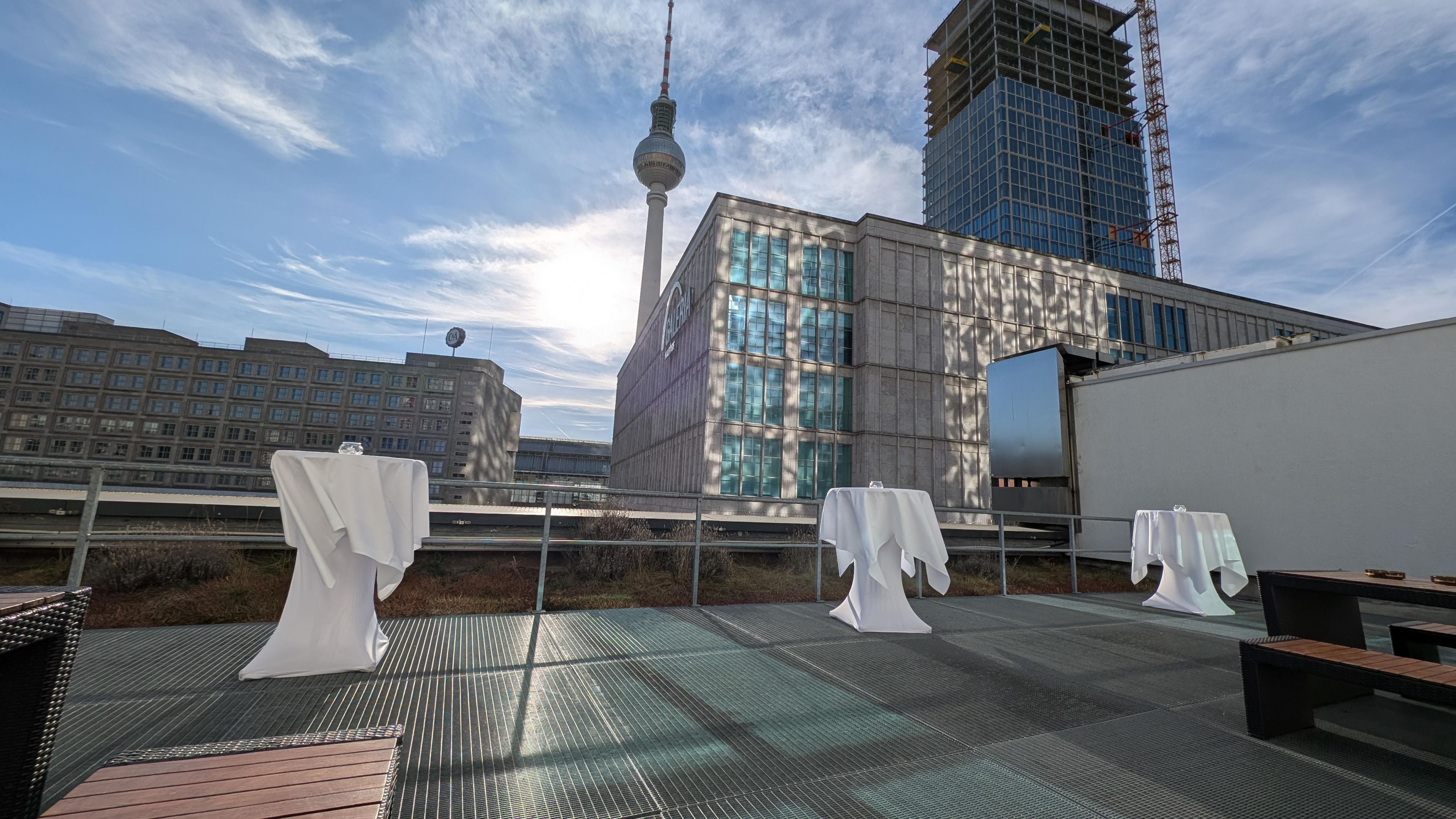 An outdoor terrace with tables and chairs, a view of a modern building, and a tower in the background.