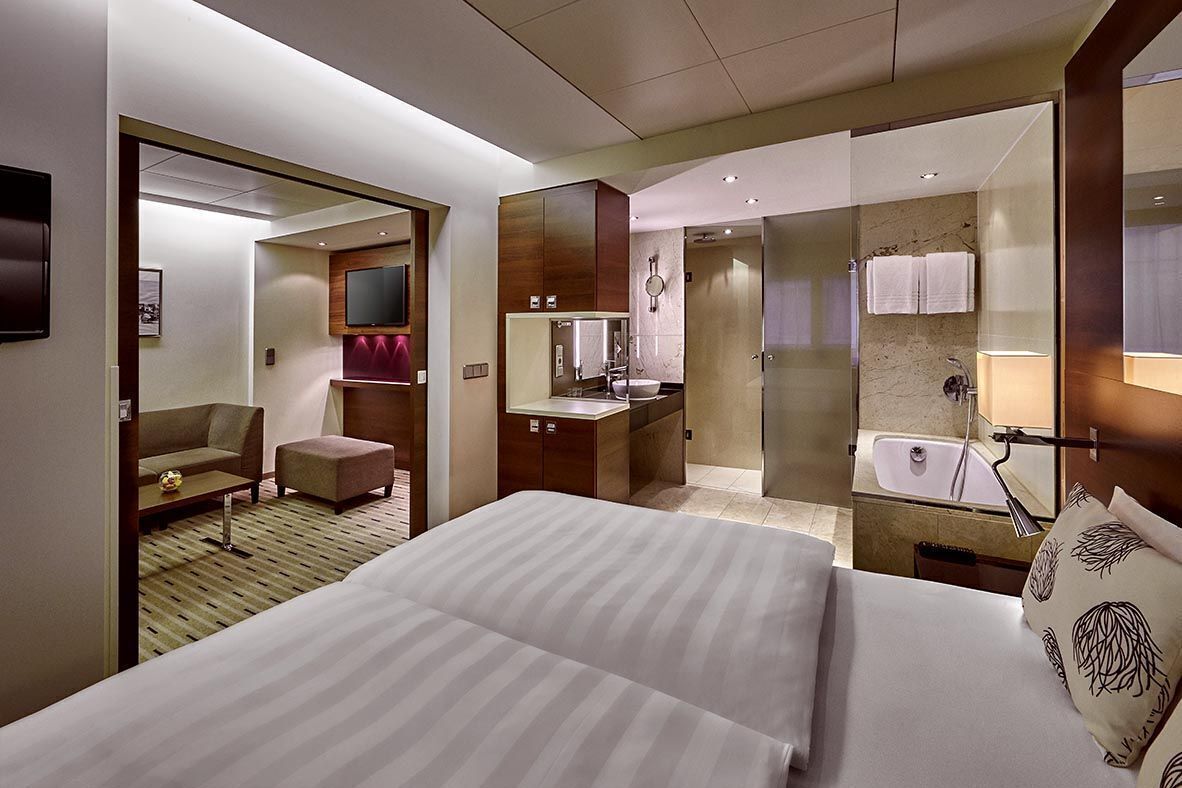 Ein Hotelzimmer mit einem großen Bett, einem Schreibtisch, einer Couch, einem Fernseher und einem Badezimmer mit Badewanne und Dusche.