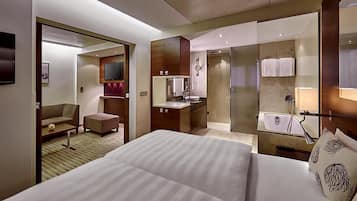 Ein Hotelzimmer mit einem großen Bett, einem Schreibtisch, einer Couch, einem Fernseher und einem Badezimmer mit Badewanne und Dusche.