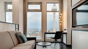 A modern living room with a sofa, two small tables, a chair, and a large window offering a city view.