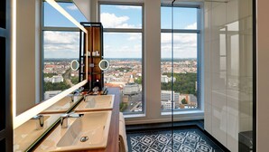 A modern bathroom with two sinks, a large mirror, and a view of a cityscape through large windows.