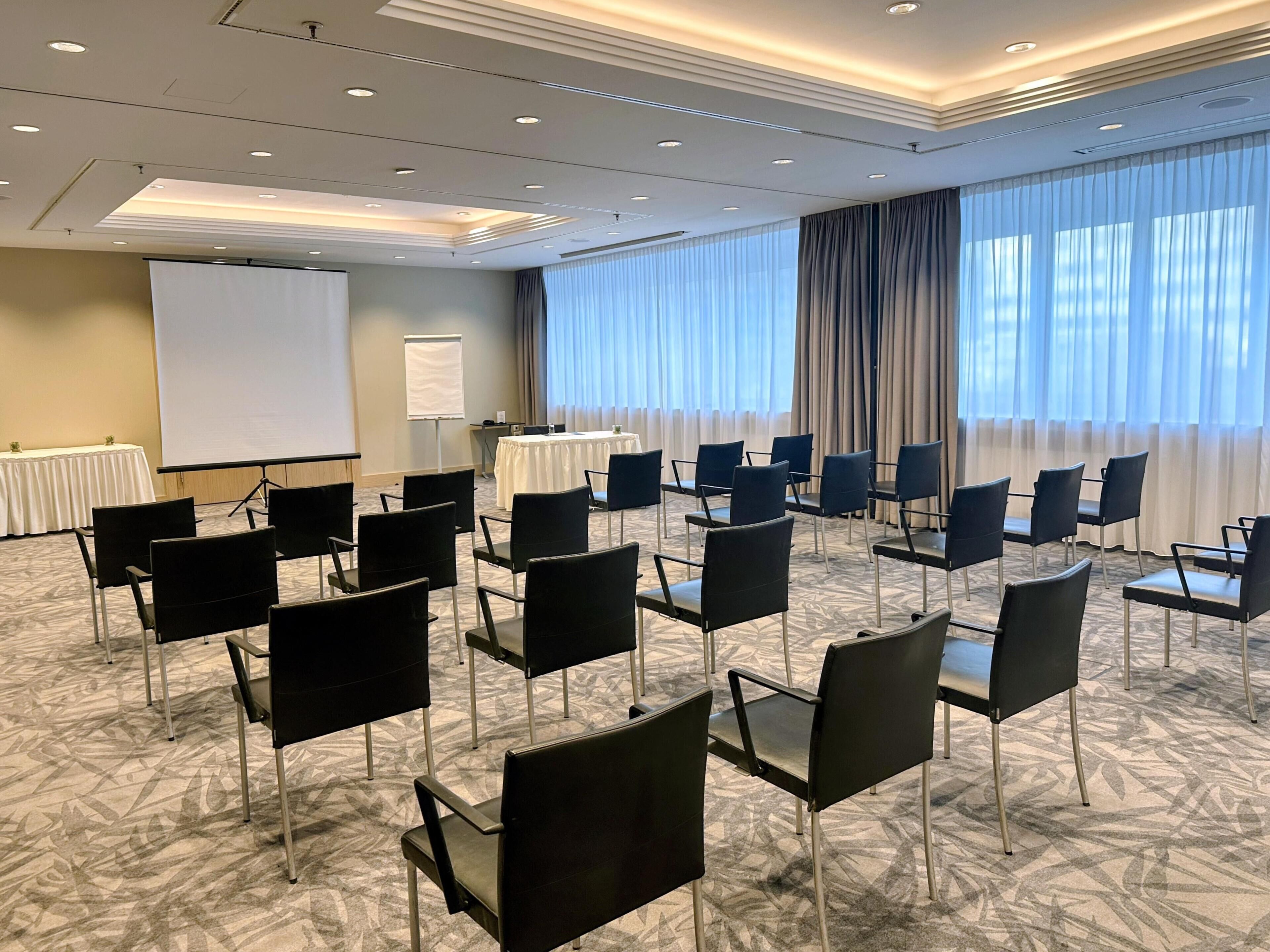 Ein Konferenzraum mit Reihen von Stühlen, einer Projektionsleinwand und einer Whiteboard-Tafel.