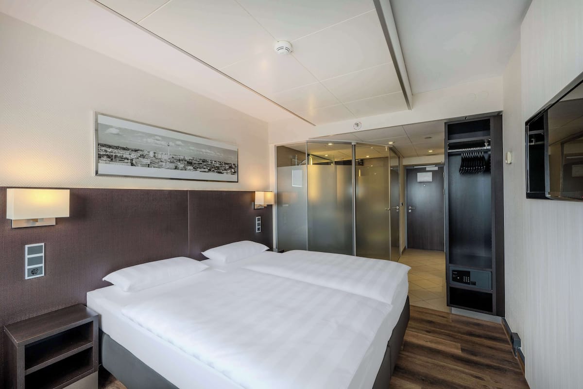Habitación de hotel con una cama grande, una mesita de noche, una lámpara de pared, un cuadro enmarcado y un armario con puerta corredera.