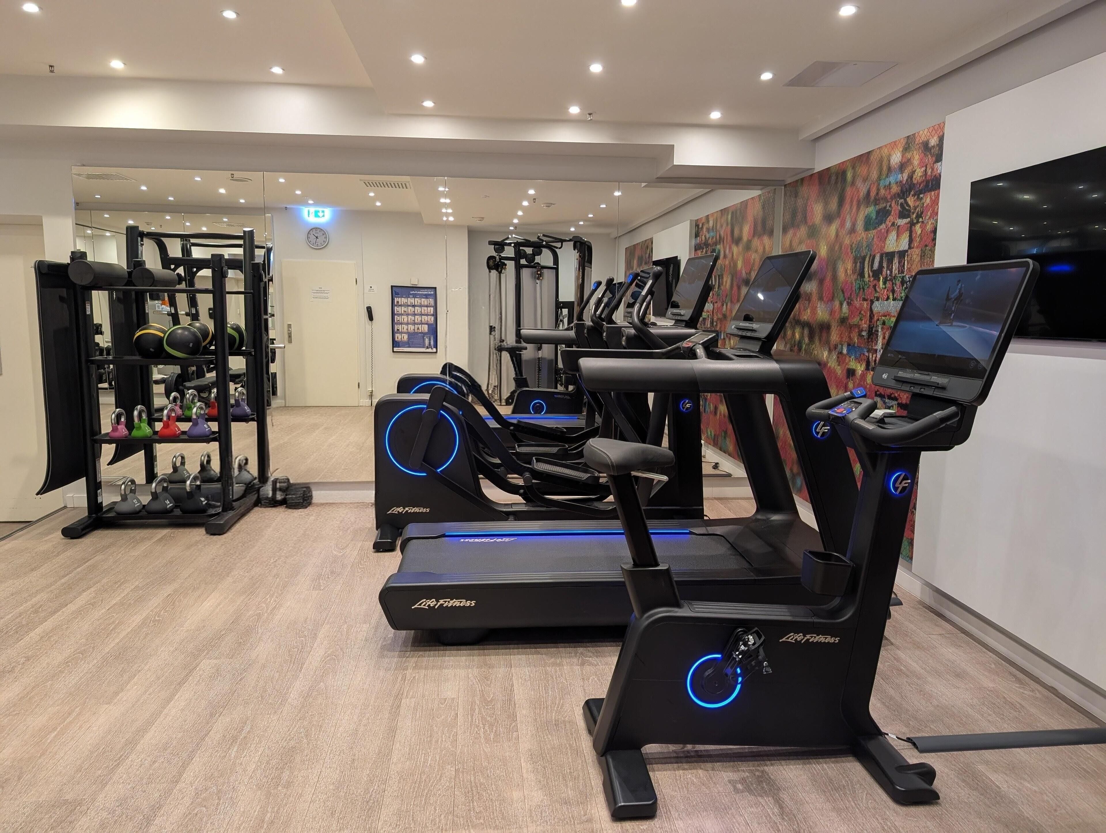 Ein Fitnessstudio mit Laufbändern, Kraftgeräten und Kurzhanteln.
