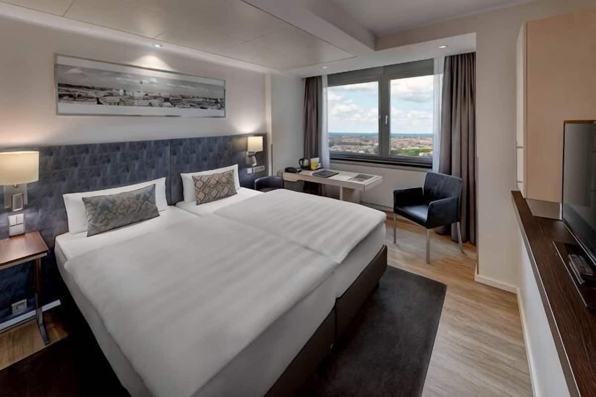 Habitación de hotel con una cama grande, un escritorio, un televisor y una ventana con vista a la ciudad.