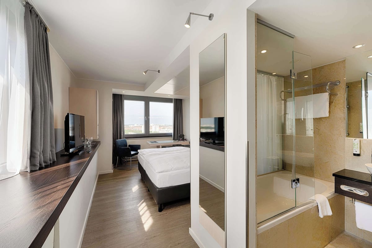 Una habitación de hotel moderna con cama, escritorio y ducha con cerramiento de vidrio.