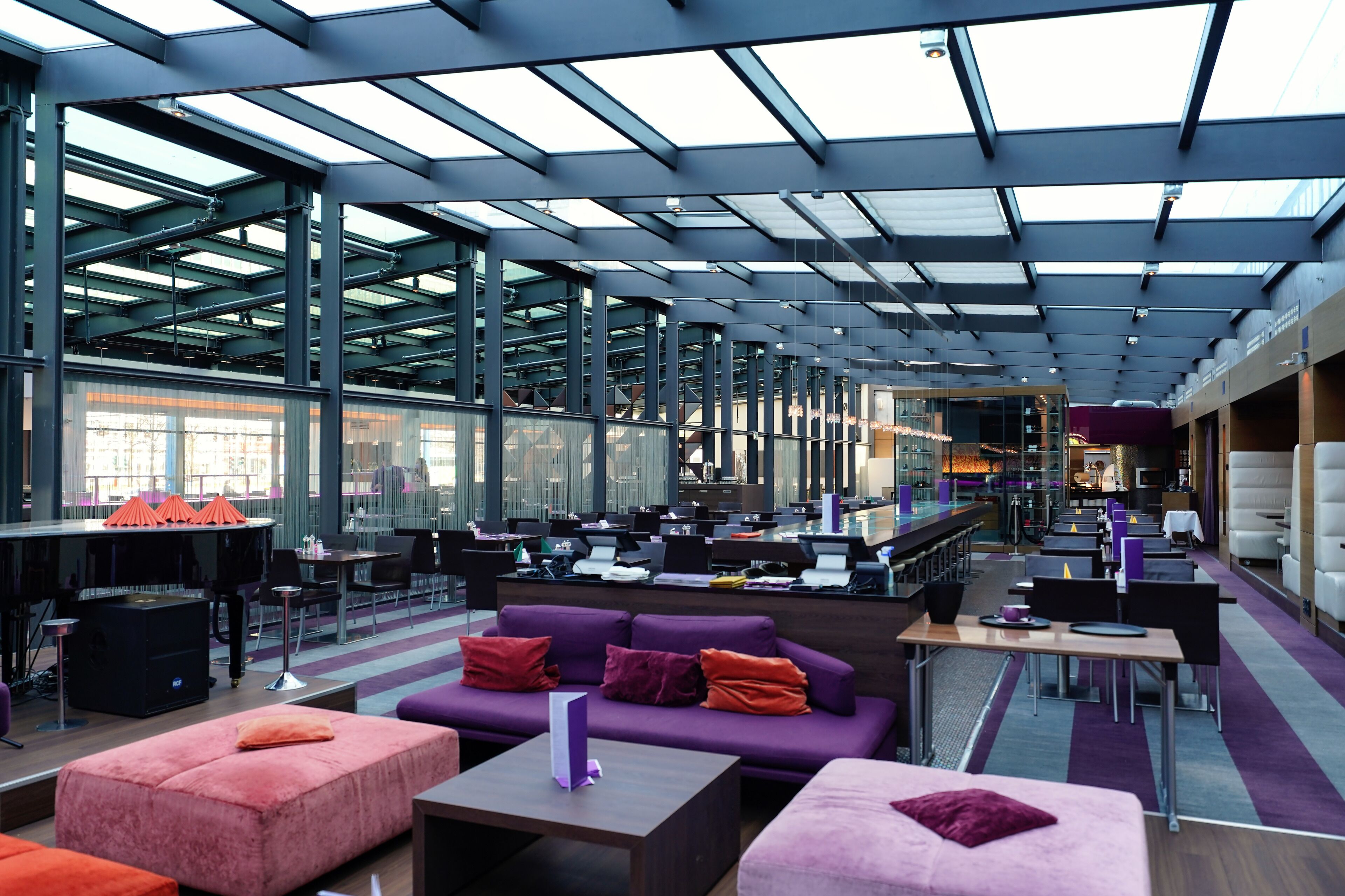 A modern interior with a high ceiling, glass walls, and a mix of seating areas including sofas and tables.