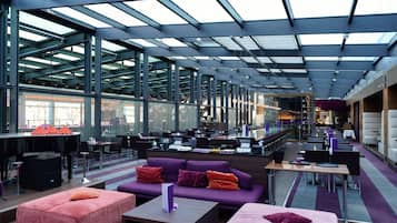 A modern interior with a high ceiling, glass walls, and a mix of seating areas including sofas and tables.