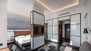 A modern hotel room with a large bed, a TV mounted on a wooden panel, a small table, and a sofa.