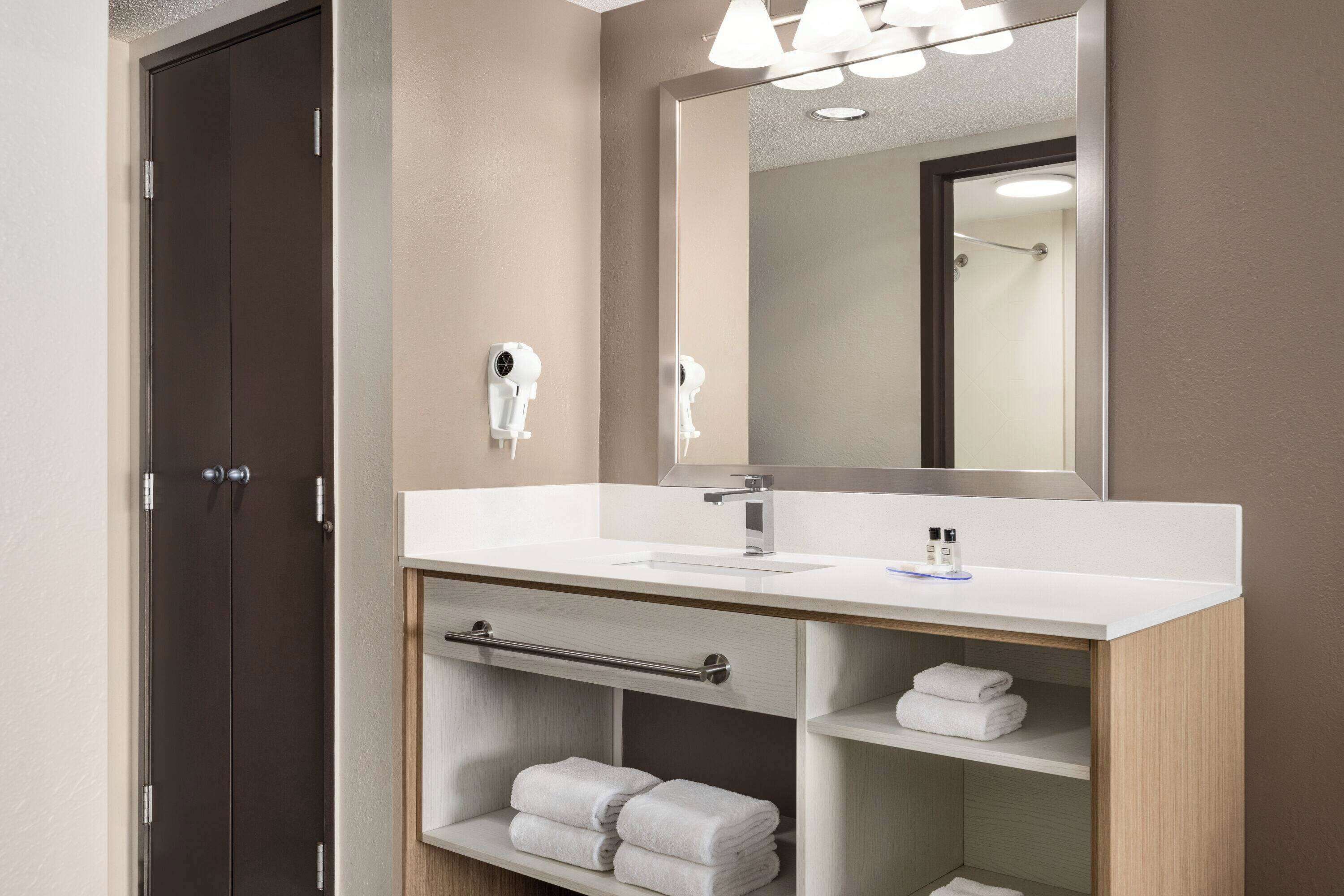 A modern bathroom with a dark wooden door, a white sink, a mirror, and a towel rack.