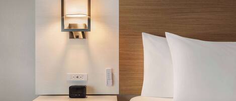 Habitación de hotel con mesita de noche, lámpara de pared, enchufe y panel de control.