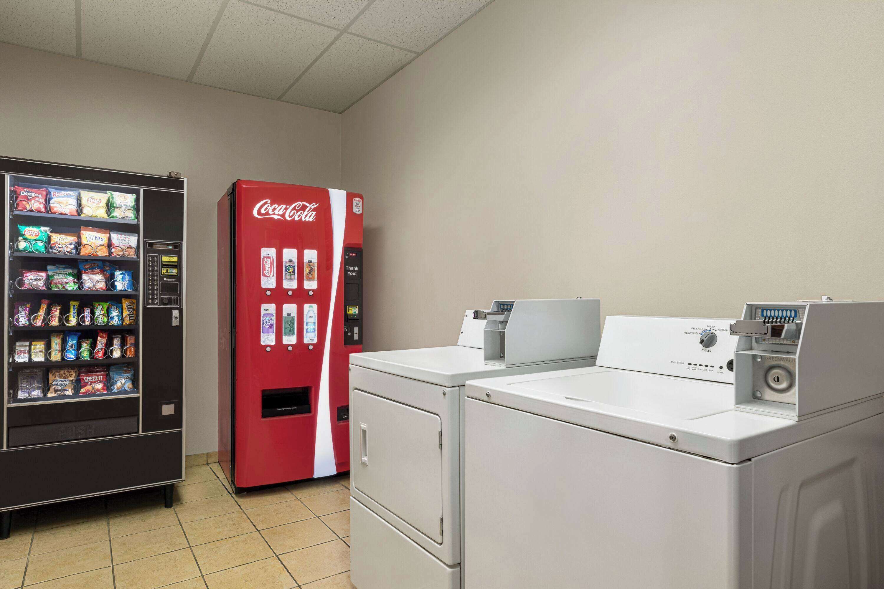 Un cuarto de lavandería con una máquina expendedora y un refrigerador rojo de Coca-Cola.
