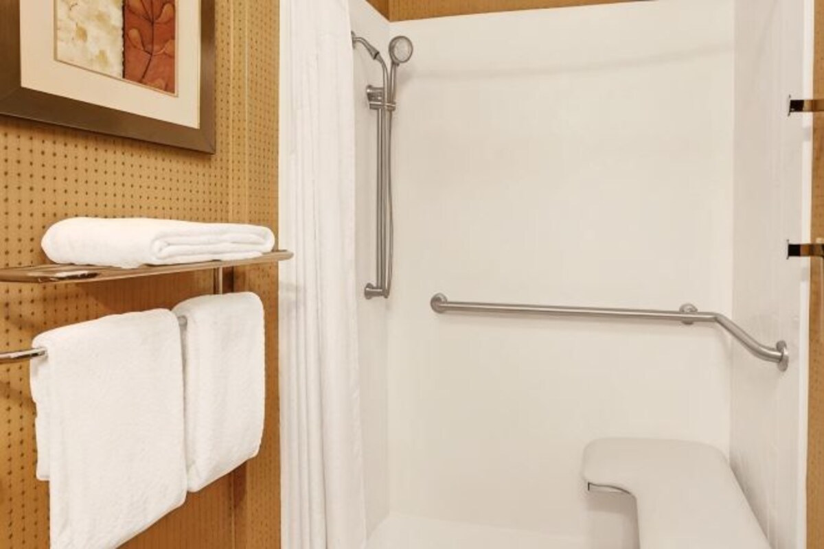 A shower with a grab bar, a toilet, and a towel rack with towels.