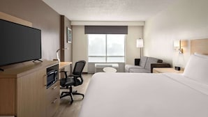 A hotel room with a bed, a desk with a computer, a chair, a television, a window with a view, and a lamp.