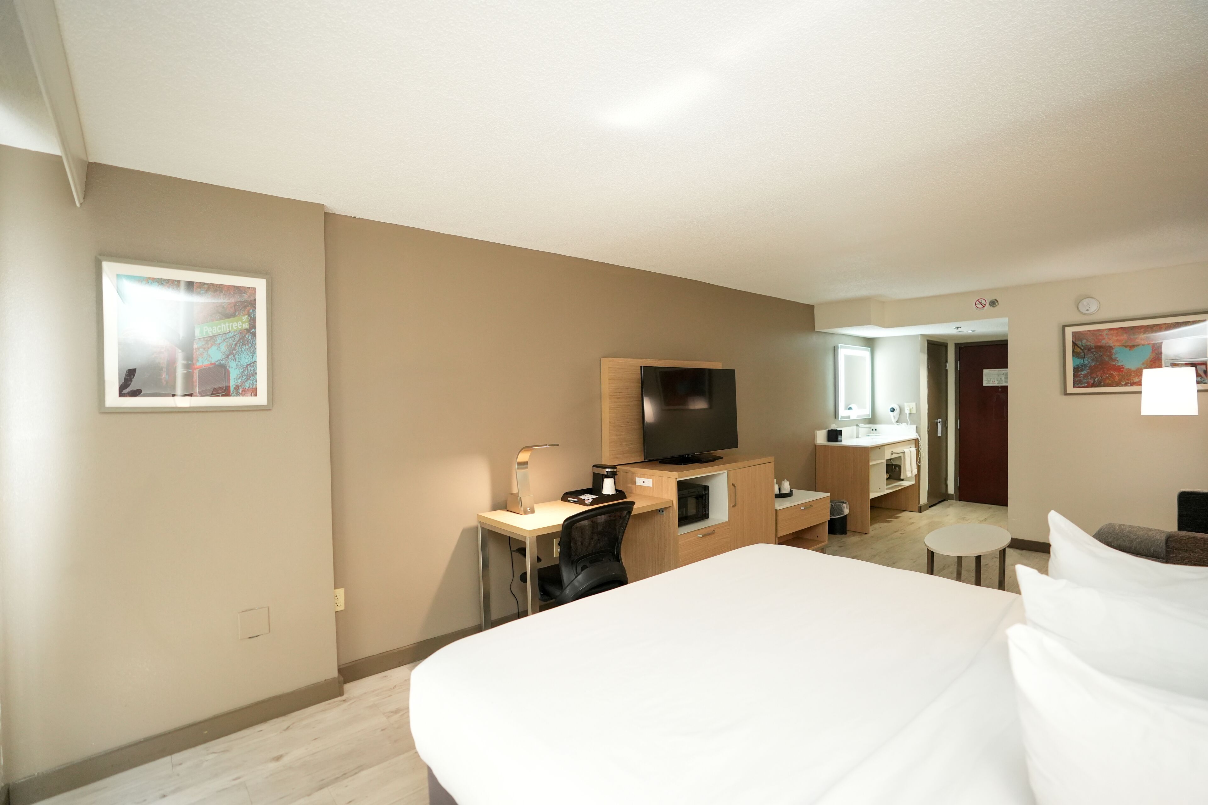 A hotel room with a bed, desk, chair, television, and a small round table.