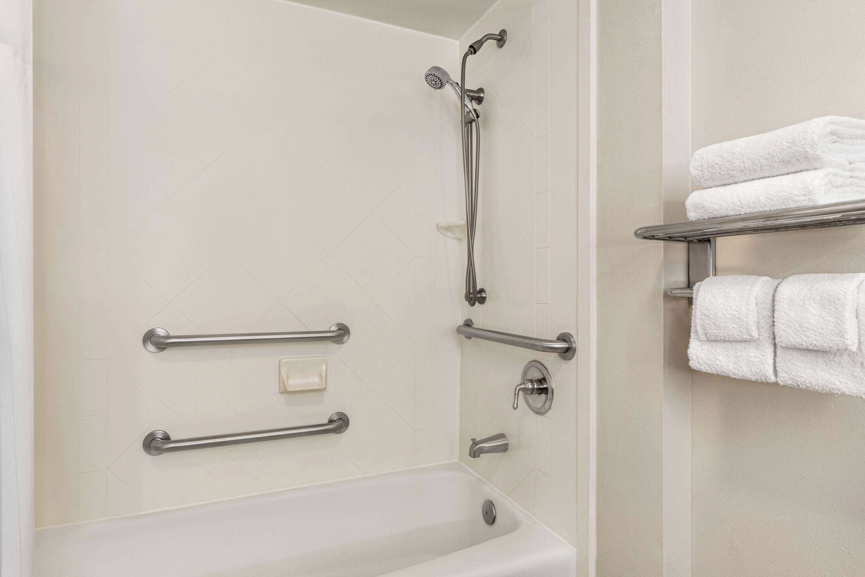 A bathroom with a bathtub, grab bars, a showerhead, and a towel rack with folded towels.