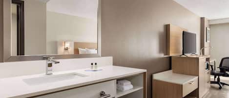 A modern bathroom with a large mirror, a sink, a vanity with shelves, and a desk area.