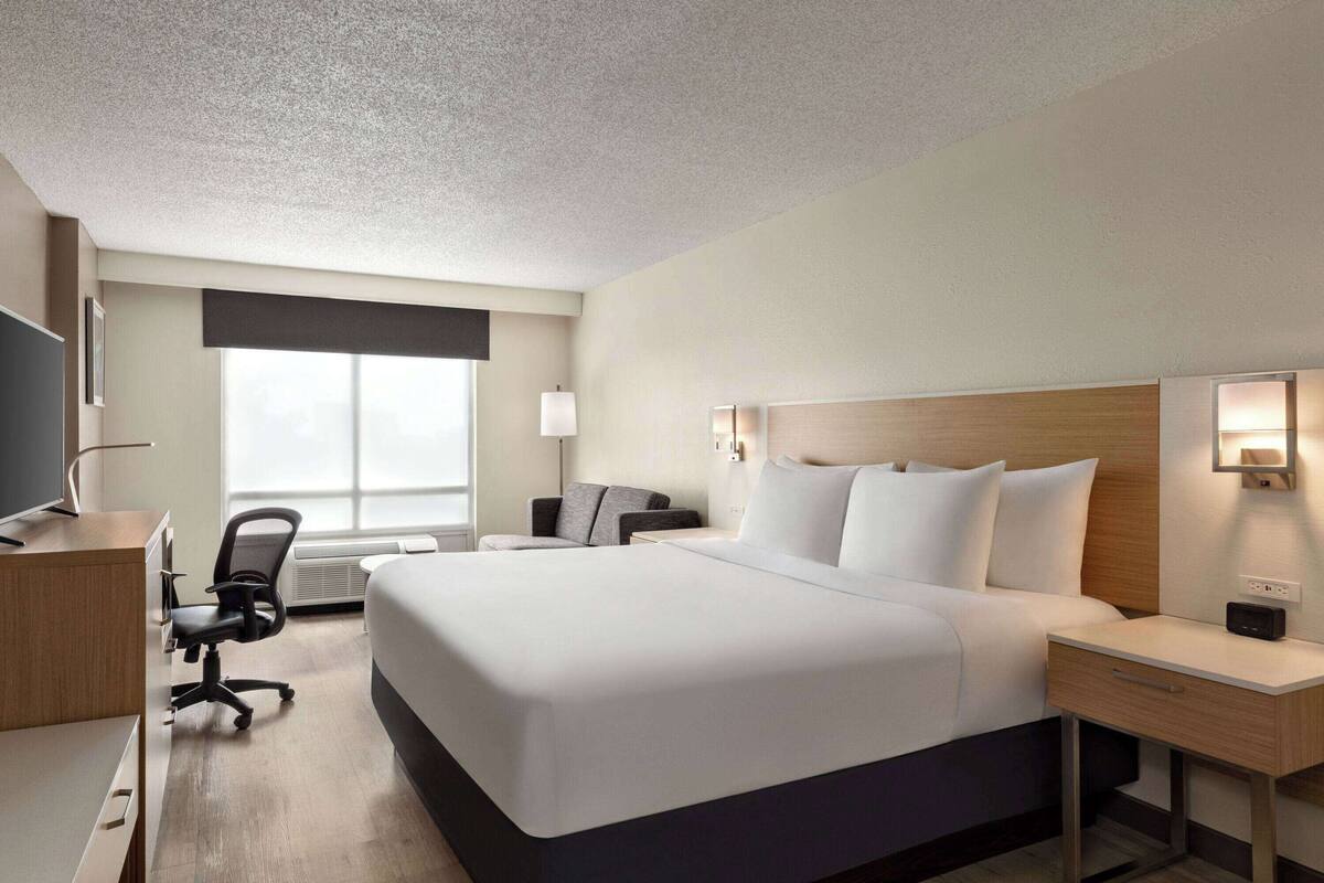 A hotel room with a large bed, a desk with a chair, a TV, and a window with a view.