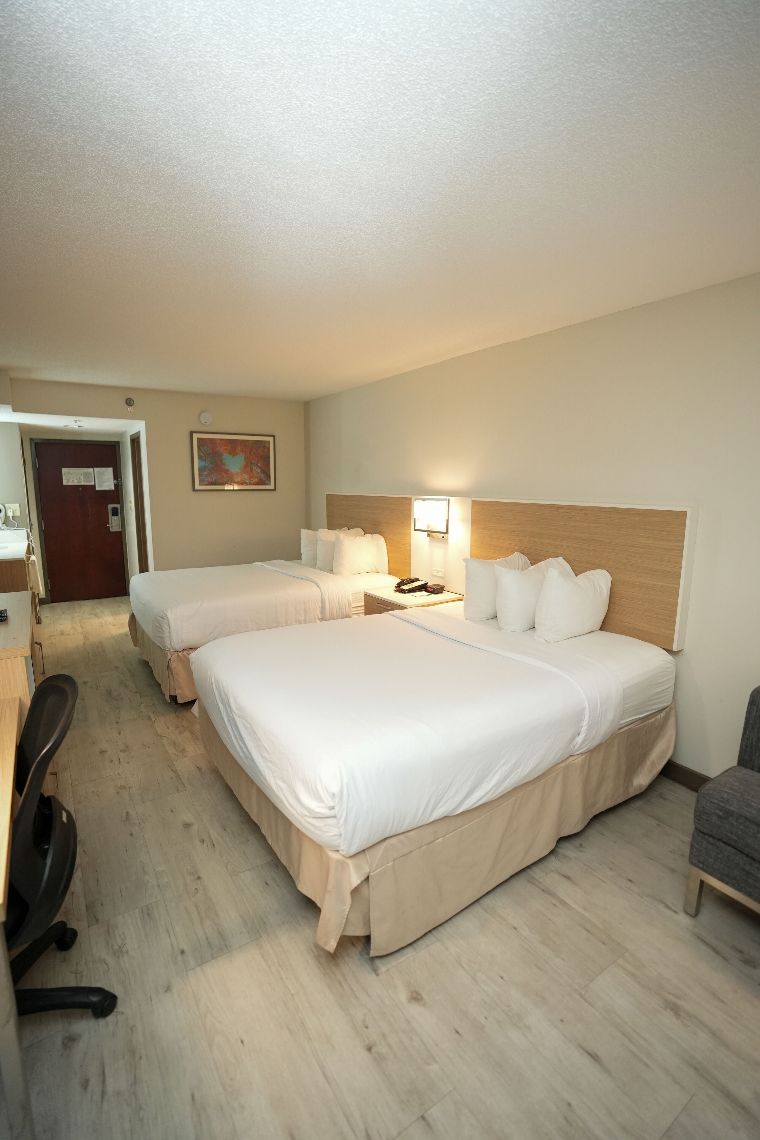 A hotel room with two beds, a desk, a chair, and a bathroom.