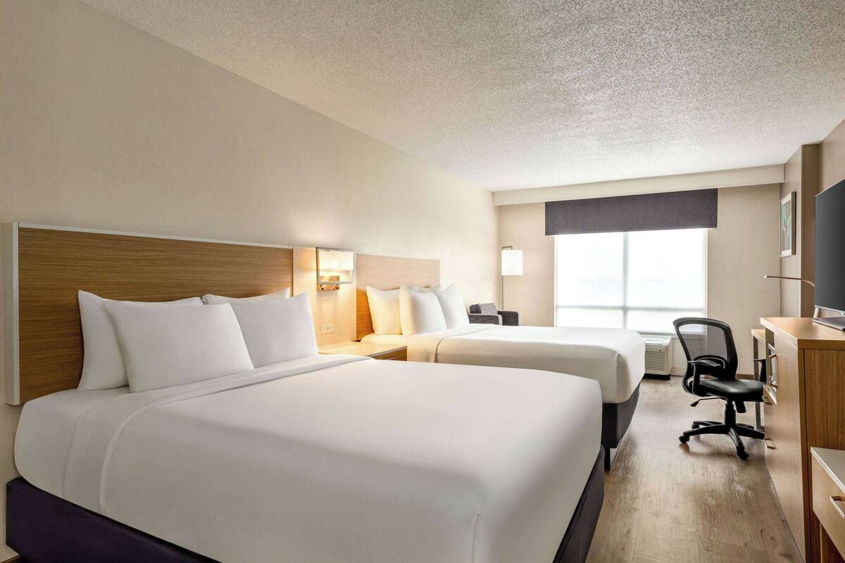 A hotel room with two beds, a desk, a chair, and a large window.