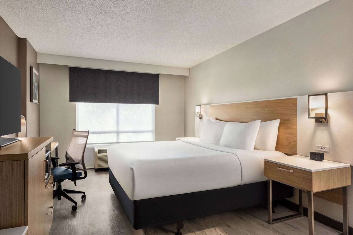A modern hotel room with a large bed, a desk, a chair, and a window with a view.