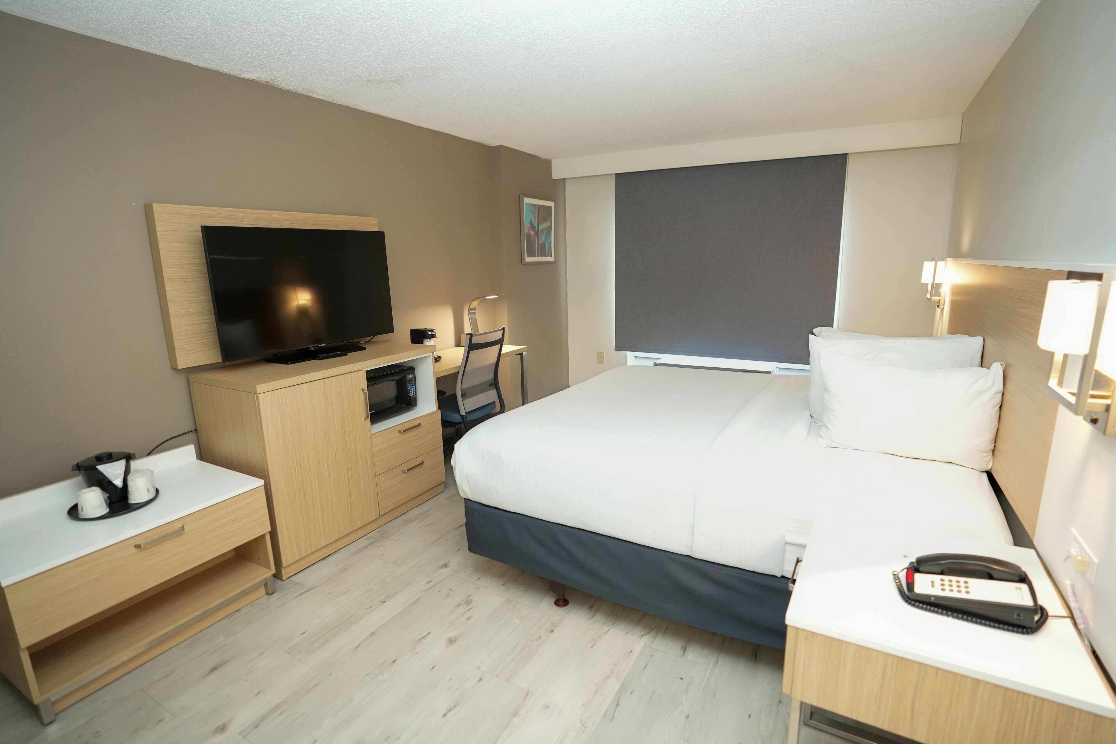 Habitación de hotel con cama, escritorio, televisión, microondas, teléfono y ventana.