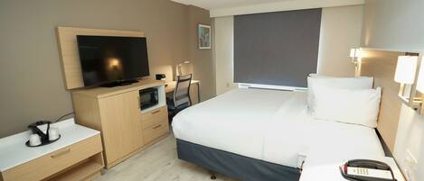 Habitación de hotel con cama, escritorio, televisión, microondas, teléfono y ventana.