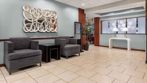 A lobby with two grey armchairs, a modern abstract wall art, a reception desk with two lamps, and a tiled floor.