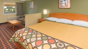 Habitación de hotel con cama, mesita de noche, silla, ventana con vistas y pared con dos cuadros enmarcados.