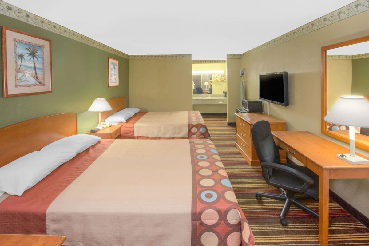 Habitación de hotel con dos camas, un escritorio, una silla, un televisor y un baño visible al fondo.
