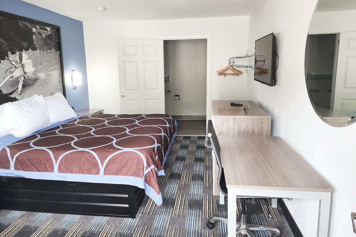 Una habitación de hotel con una cama, un escritorio, un espejo y una puerta que da a otra habitación.
