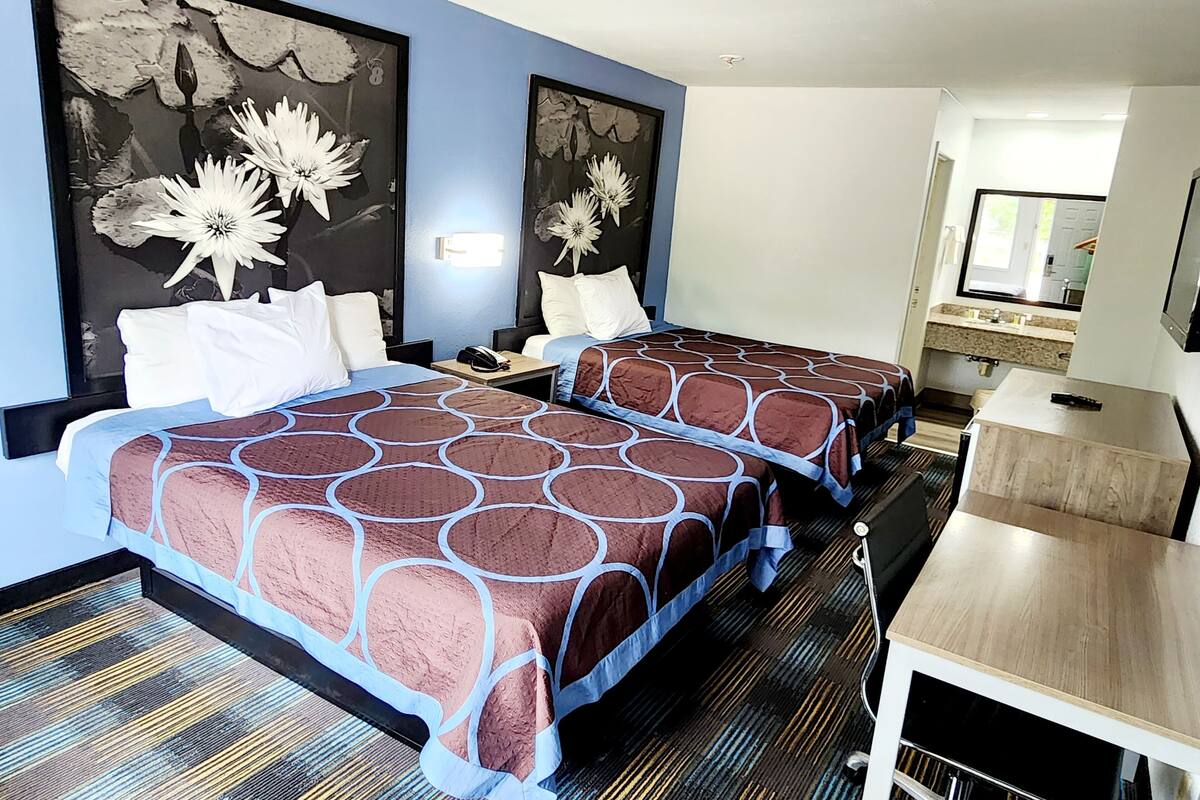 Una habitación de hotel con dos camas, un escritorio, un espejo y obras de arte en las paredes.