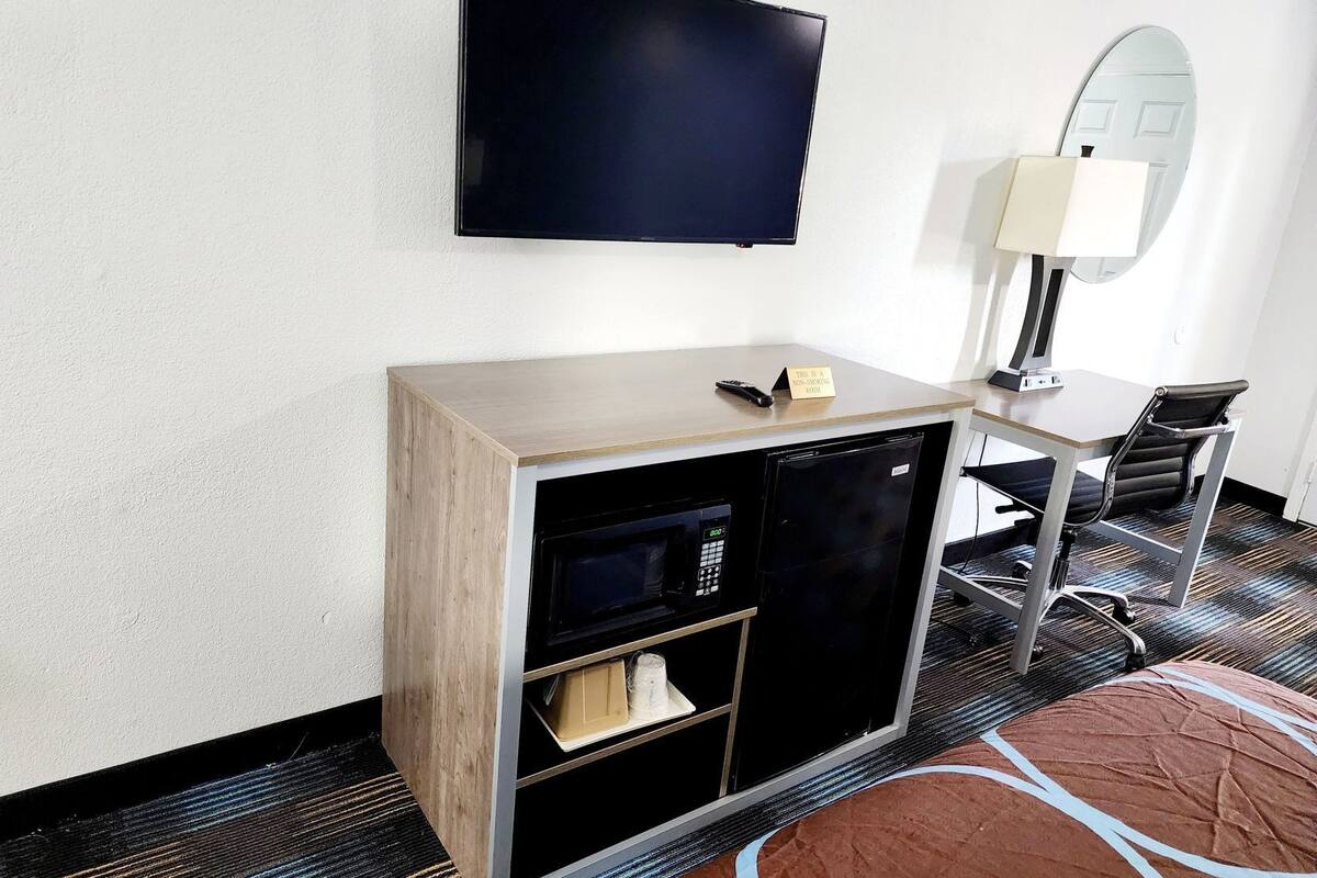 Habitación de hotel con televisión de pantalla plana, escritorio con silla, lámpara y minibar.