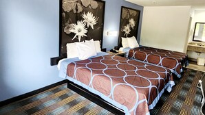 Habitación de hotel con dos camas, una mesita de noche, un espejo y un baño con lavamanos e inodoro.