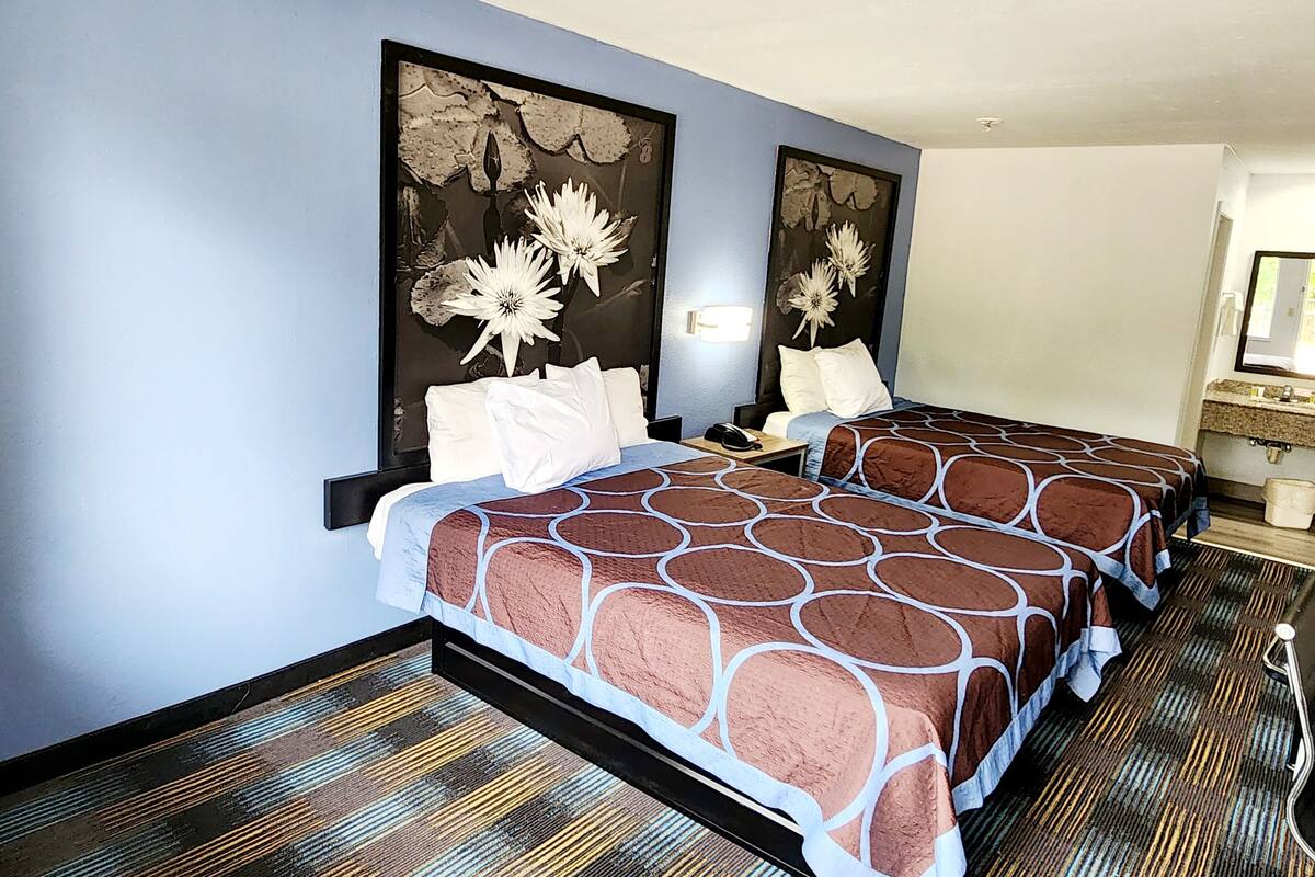 Habitación de hotel con dos camas, una mesita de noche, un espejo y un baño con lavamanos e inodoro.