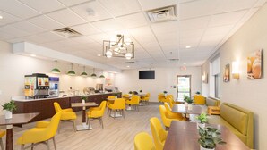 A modern dining area with yellow chairs, wooden tables, and a central counter with a coffee machine. - Comfort Inn & Suites Buffalo Airport (Buffalo)