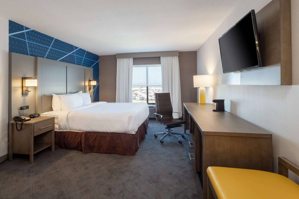 A hotel room with a large bed, a desk, a chair, a TV, and a view of the city.