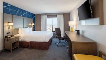 A hotel room with a large bed, a desk, a chair, a TV, and a view of the city.