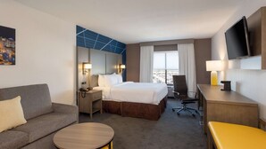 A hotel room with a bed, a desk, a chair, a sofa, a small round table, and a TV mounted on the wall. - Comfort Inn & Suites Buffalo Airport (Buffalo)