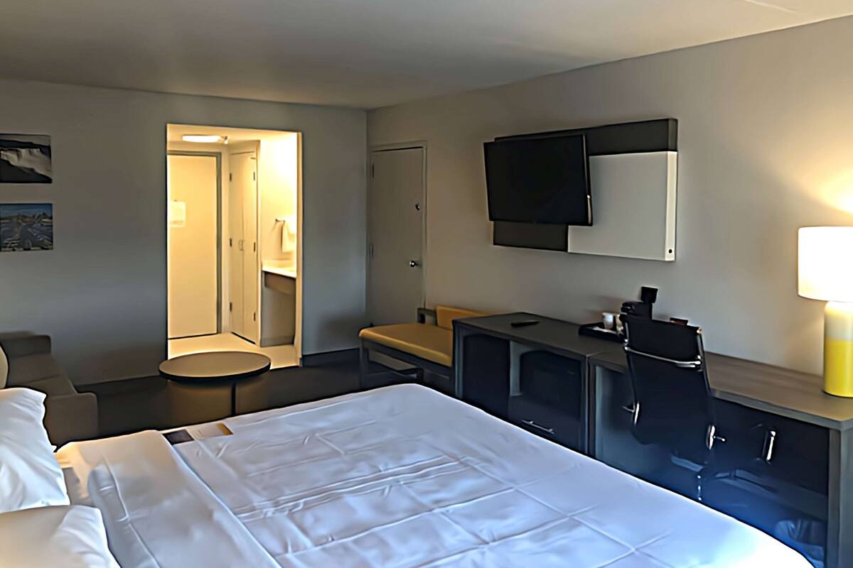 A hotel room with a bed, a desk, a TV, and a bathroom visible through an open door.