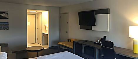 A hotel room with a bed, a desk, a TV, and a bathroom visible through an open door.