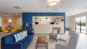 A modern hotel lobby with a blue accent wall, a reception desk, a sofa, a chair, and a coffee table. - Comfort Inn & Suites Buffalo Airport (Buffalo)
