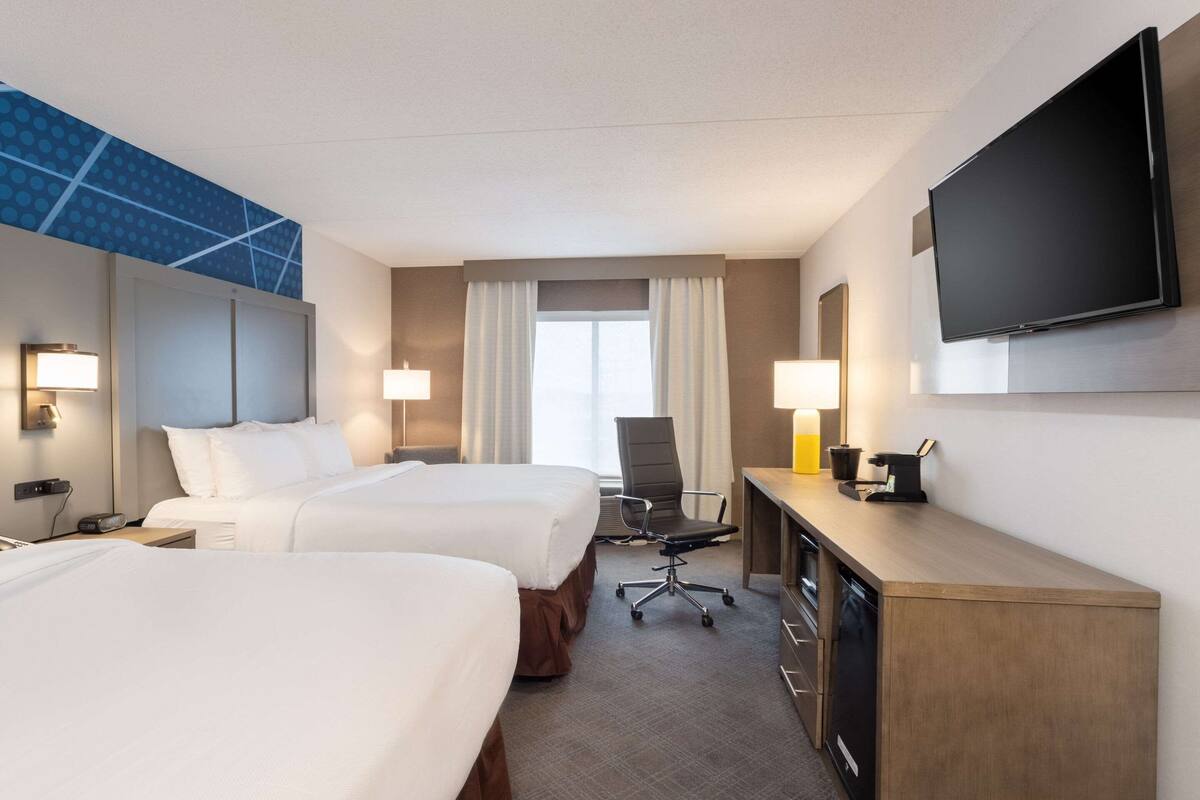 A hotel room with two beds, a desk with a flat-screen TV, a chair, and a desk lamp.