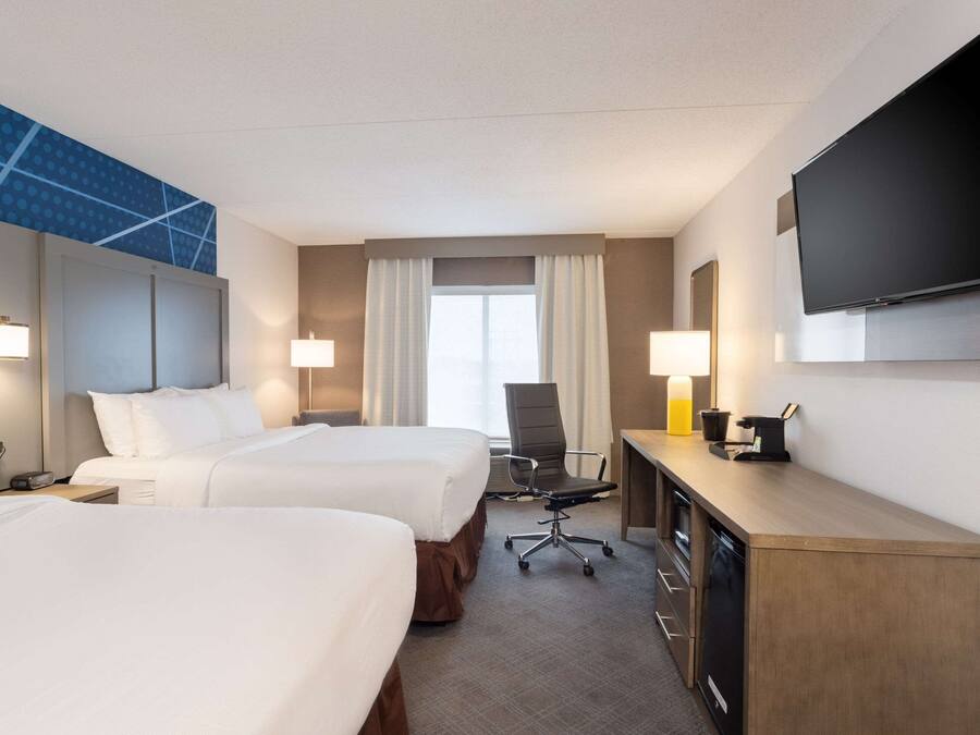 Habitación de hotel con dos camas, un escritorio, una televisión de pantalla plana, una silla y una lámpara de escritorio.