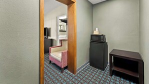 A hotel room with a patterned floor, a wooden door frame, a small black TV stand, a microwave, and a pink chair.